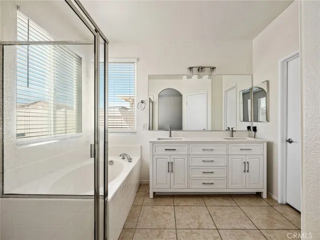 Step into this refreshed primary bath featuring a new dual-sink vanity, sleek tile floors, and updated lighting that adds a modern touch while providing comfort and convenience. Features separate shower and garden tub.