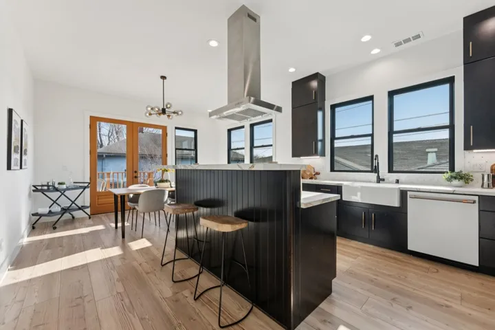 Kitchen with a kitchen bar, dark cabinets, white dishwasher, and light wood-style flooring