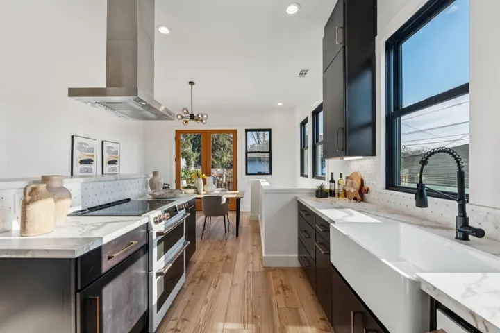 Dual tone kitchen featuring double oven range, range hood, dual tone cabinets, light wood-type flooring, and suspended lighting