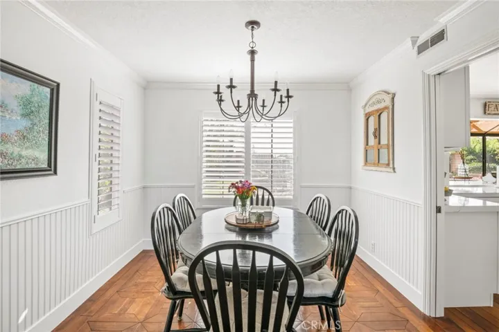 Spacious dining room with view to rear yard through plantation shutters is located between living room and kitchen for convenient meal serving. Notice the wainscoting and pocket door.