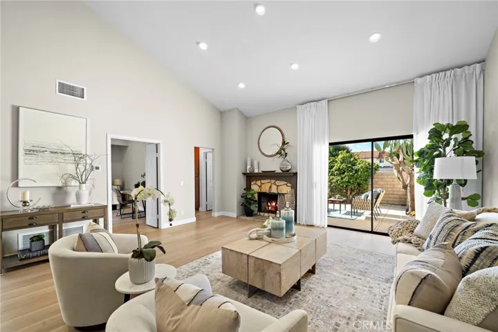 Spacious, light, and bright living room with soaring ceiling, stone fireplace, recessed lighting, and slider that leads to large patio