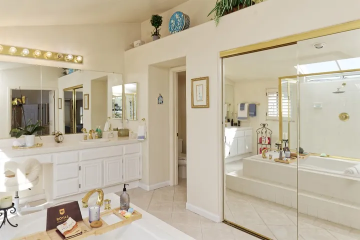 Full bath featuring a bath, vanity, a tile shower, light tile patterned flooring, and vaulted ceiling