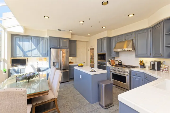 Kitchen with tile counters, open shelves, stainless steel appliances, a kitchen island, and tasteful backsplash
