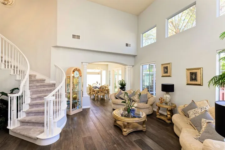 Living area with ornate columns, dark wood-style flooring, arched walkways, and a high ceiling