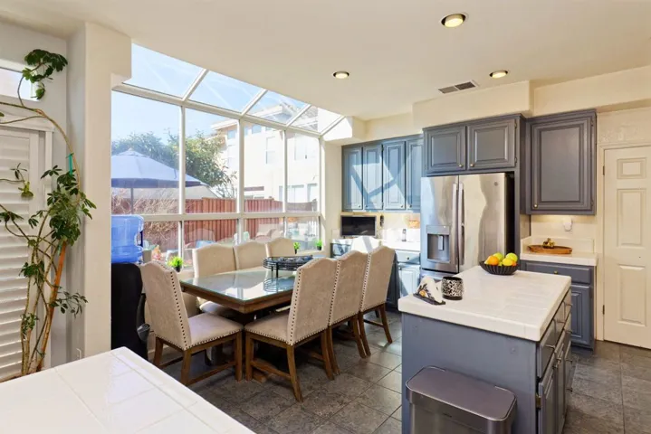 Kitchen featuring tile countertops, stainless steel fridge with ice dispenser, a kitchen island, a sunroom, and recessed lighting