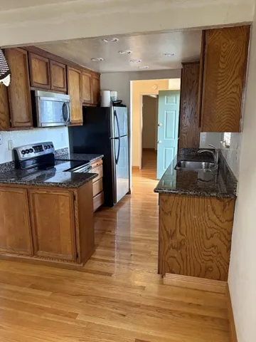 Kitchen with dark stone counters, wood finish cabinetry, a peninsula, and stainless steel appliances