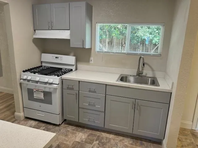 Kitchen with gray cabinets, white gas range, light countertops, under cabinet range hood, and a textured wall