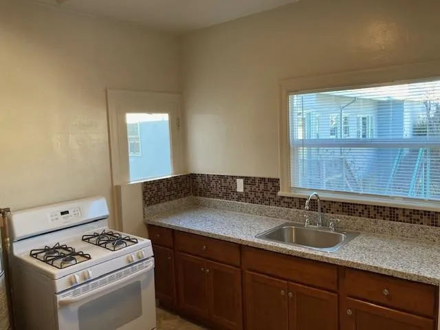 Kitchen featuring gas range gas stove, light stone countertops, brown cabinetry, and tasteful backsplash