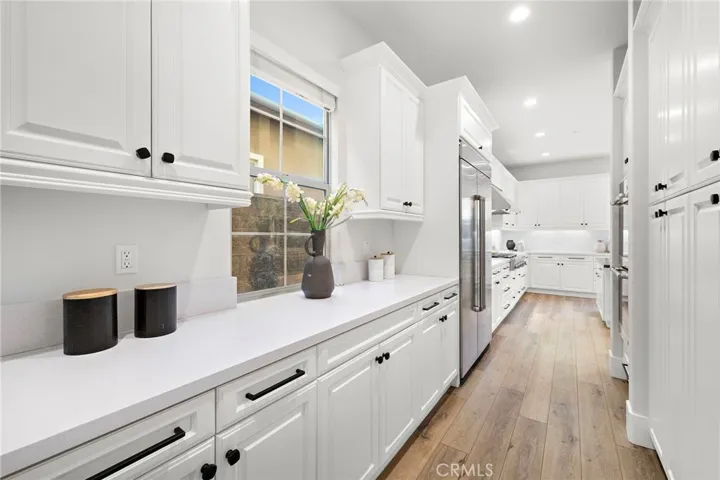 Kitchen detail featuring custom cabinetry, designer range hood, built-in dual ovens, and built-in refrigerator

