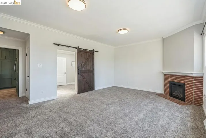 Unfurnished living room with crown molding, a barn door, carpet, and a fireplace