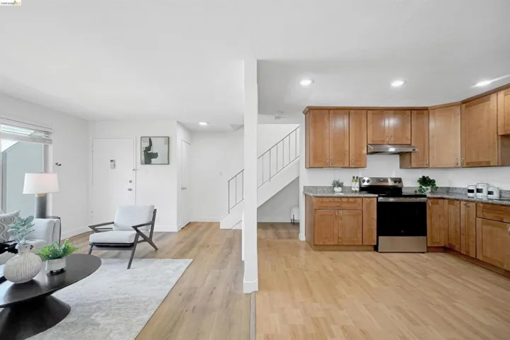 Kitchen with stainless steel electric stove, wood finish cabinetry, light wood-type flooring, light stone counters, and recessed lighting