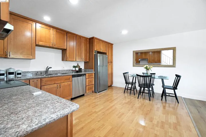 Kitchen with wood finish cabinets, light stone counters, dishwasher, freestanding refrigerator, and recessed lighting