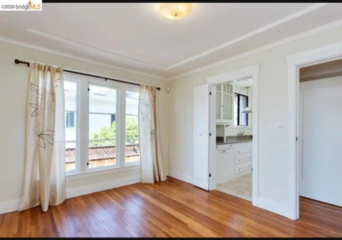 Unfurnished bedroom featuring light wood-style floors, ensuite bathroom, and ornamental molding
