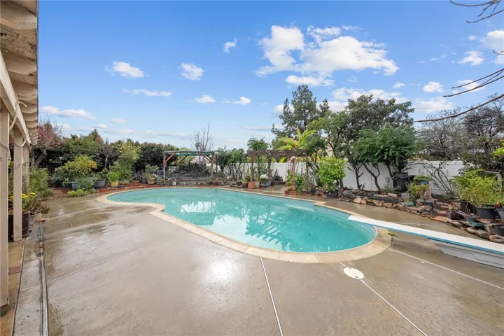 Wide backyard view featuring the pool, surrounding hardscape, and lush garden beds/planters.