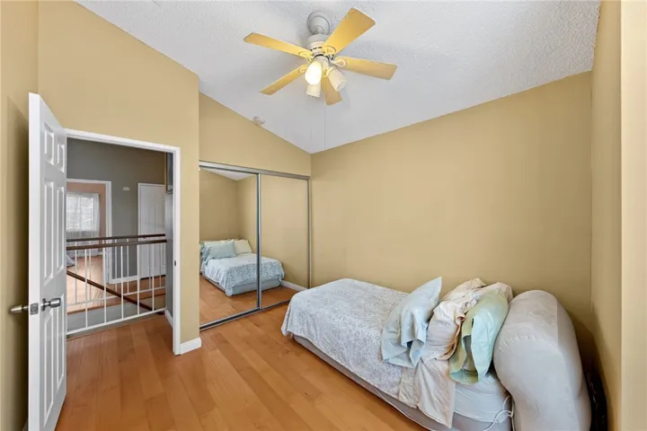 Bedroom with mirrored closet doors, ceiling fan, and hardwood flooring with open hallway access.