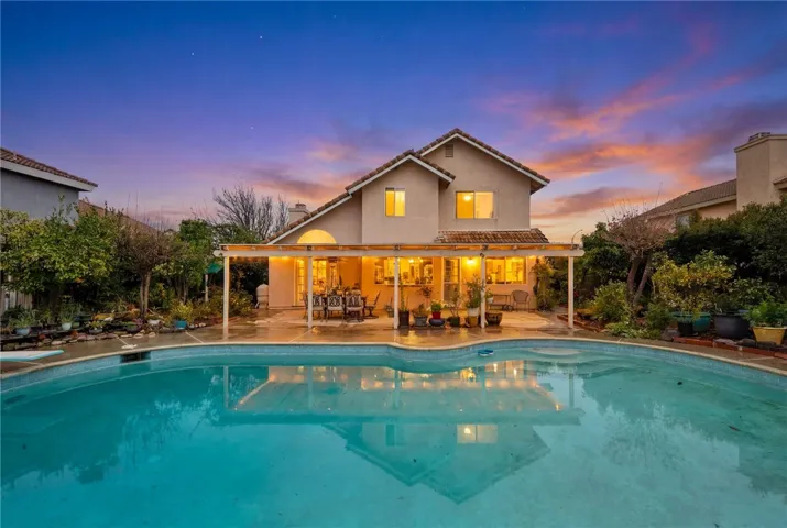 Wide pool-side view of the covered patio and outdoor living area with ambient lighting and mature plantings.
