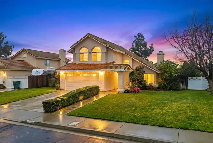 Twilight curb view featuring a well-kept lawn, tile roof, and illuminated windows for a warm evening presence.
