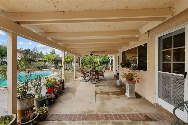 Covered patio corridor with seating and potted plants, offering shaded outdoor living beside the pool.