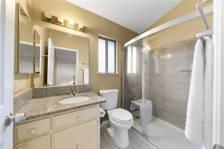 Full bath with vanity, large mirror, and glass-enclosed shower with tile surround.
