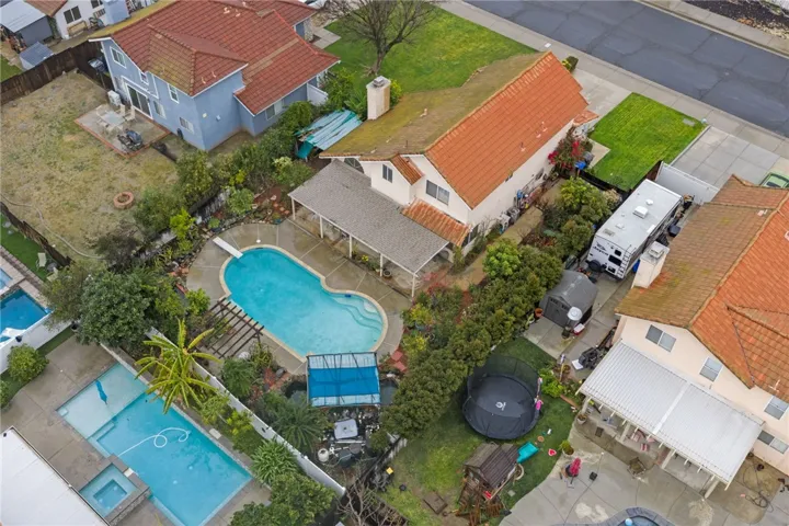 Angled drone view showcasing the home’s footprint, covered patio, and pool area with mature greenery and fencing.
