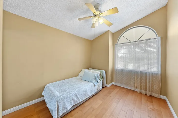Light-filled bedroom with vaulted ceiling, ceiling fan, and large arched window for added character.
