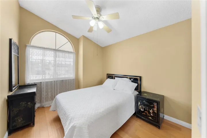 Cozy bedroom with vaulted ceiling, ceiling fan, arched window, and classic built-in style nightstands/dresser.