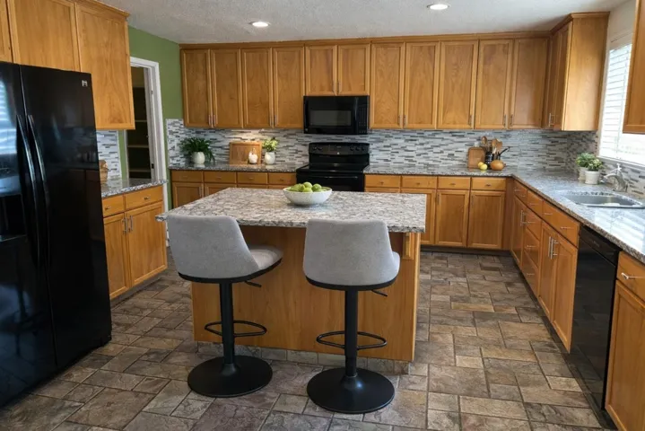 Kitchen featuring black appliances, a kitchen island, light stone counters, wood finish cabinetry, and a kitchen bar