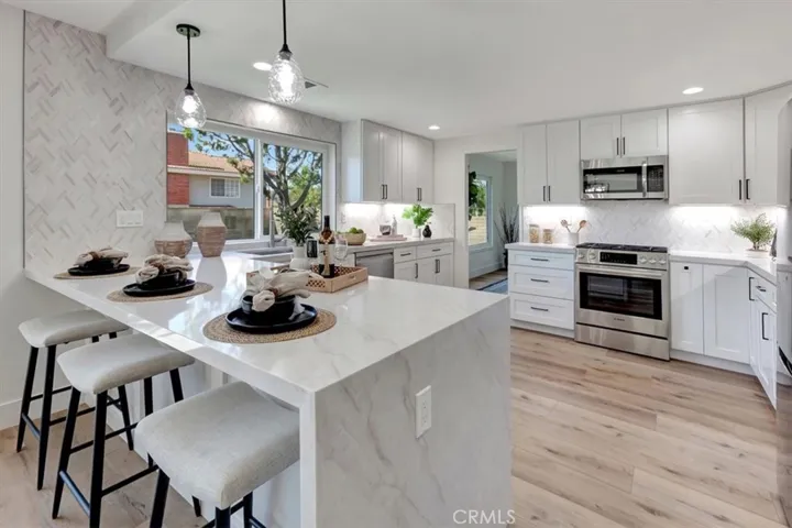 The chef’s kitchen is a true showpiece, featuring white shaker cabinetry, Ivory Taj quartz countertops with waterfall peninsula, honed marble backsplash, under cabinet, recessed & pendant lighting.