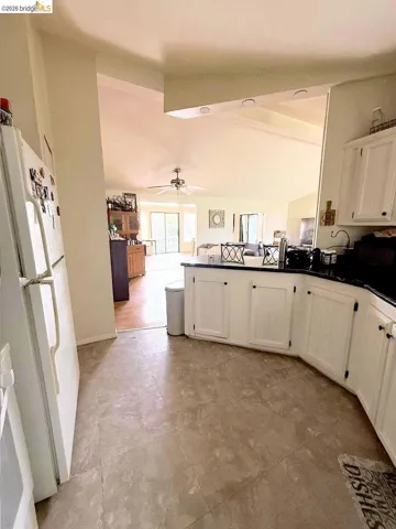 Kitchen with dark countertops, freestanding refrigerator, vaulted ceiling, a peninsula, and open floor plan