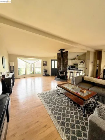 Living area featuring light wood-type flooring, a wood stove, and vaulted ceiling with beams