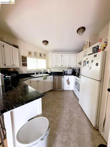 Kitchen with white appliances, white cabinetry, a peninsula, and tile counters