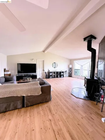 Living room with a wood stove, beamed ceiling, and light wood-style flooring