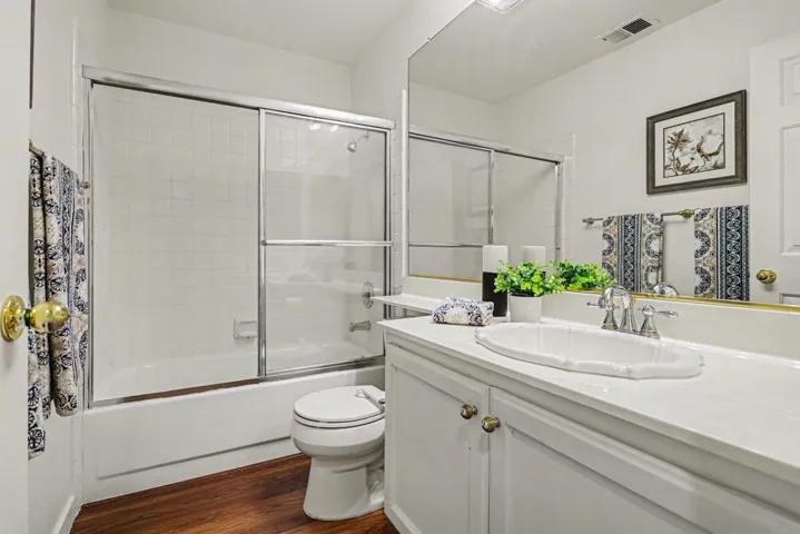 Bathroom with vanity, bath / shower combo with glass door, and dark wood-style flooring