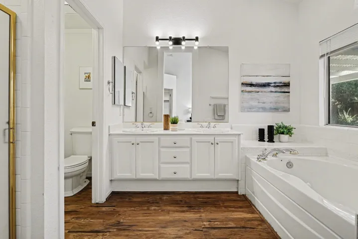 Full bath featuring dark wood finished floors, double vanity, a garden tub, and an enclosed shower