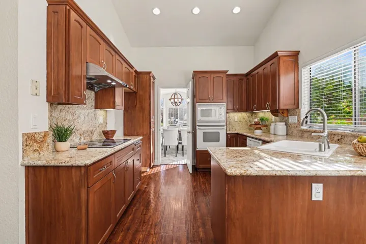 Kitchen featuring light stone countertops, dark wood-type flooring, white appliances, recessed lighting, and decorative backsplash