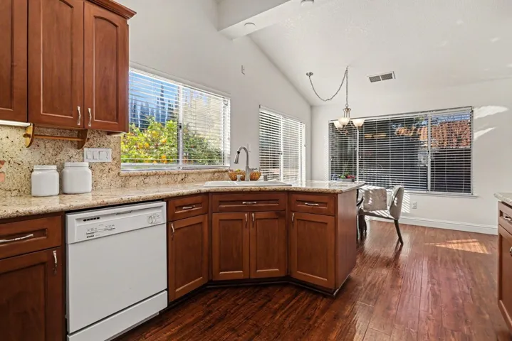Kitchen with dishwasher, a peninsula, lofted ceiling, dark wood finished floors, and wood finish cabinetry