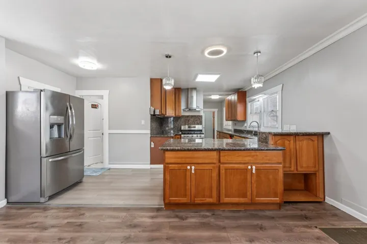 Kitchen with wood finish cabinetry, a peninsula, stainless steel appliances, dark stone countertops, and dark wood-style floors
