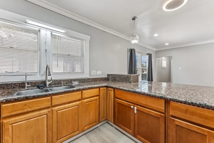 Kitchen with wood finish cabinets, dark stone countertops, crown molding, light wood-style floors, and hanging light fixtures