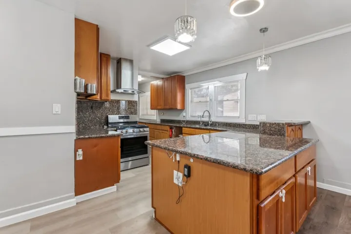 Kitchen featuring wood finish cabinets, dark stone counters, gas range, a peninsula, and hanging light fixtures
