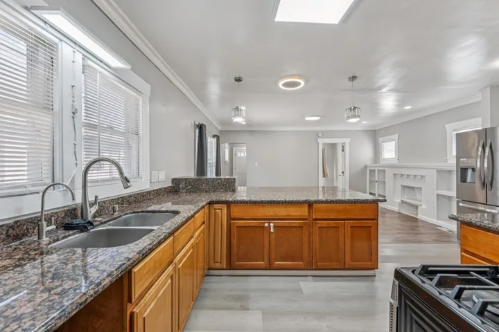 Kitchen with a peninsula, ornamental molding, wood finish cabinetry, pendant lighting, and light wood-type flooring