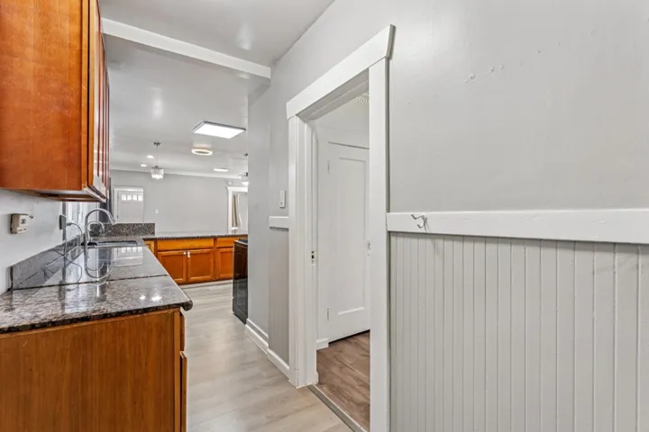 Kitchen featuring dark stone countertops, light wood-style flooring, wood finish cabinets, a wainscoted wall, and a peninsula