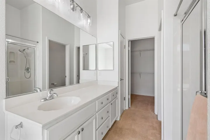 Full bath with a shower stall, vanity, light colored carpet, and a walk in closet