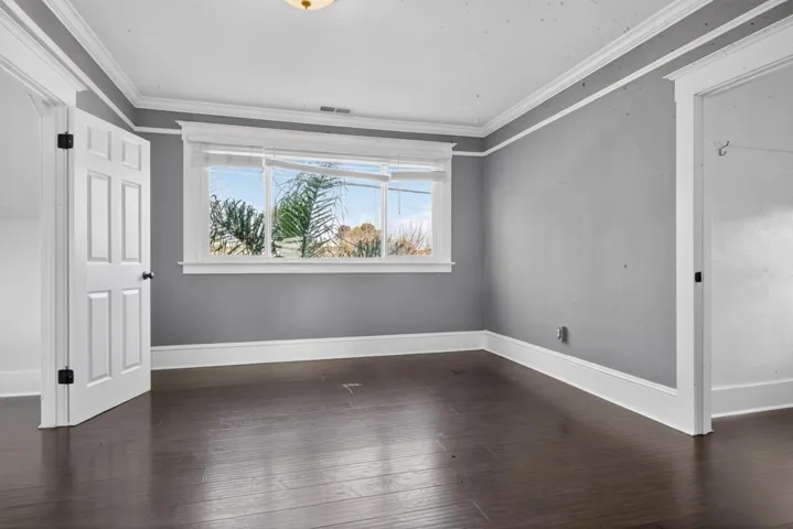 Unfurnished room with crown molding and dark wood-type flooring