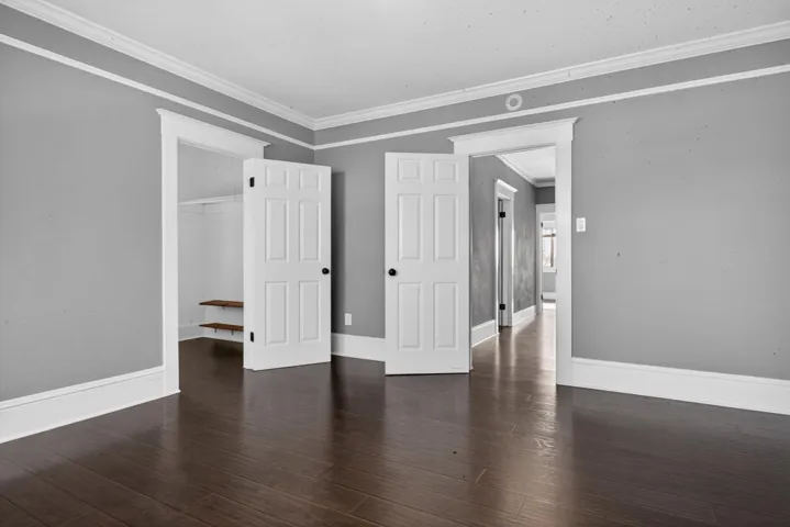 Unfurnished bedroom with ornamental molding, a closet, and dark wood finished floors
