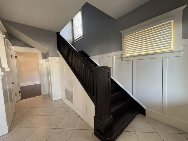 Stairway featuring a decorative wall, wainscoting, and tile patterned floors