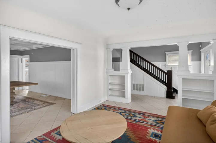 Living area with a wainscoted wall, light tile patterned flooring, a decorative wall, and ornate columns