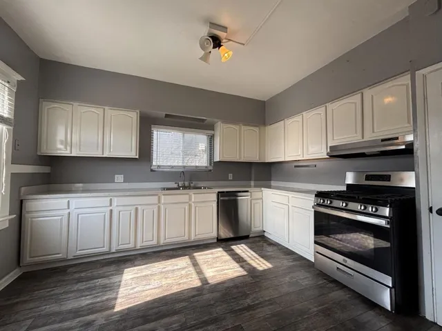 Kitchen featuring stainless steel appliances, dark wood finished floors, light countertops, white cabinetry, and ceiling fan