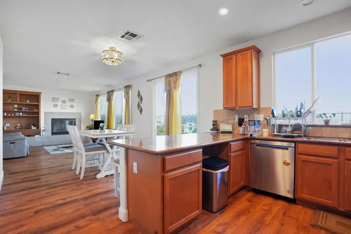 Kitchen featuring wood finish cabinets, a peninsula, open floor plan, dishwasher, and dark wood-style flooring