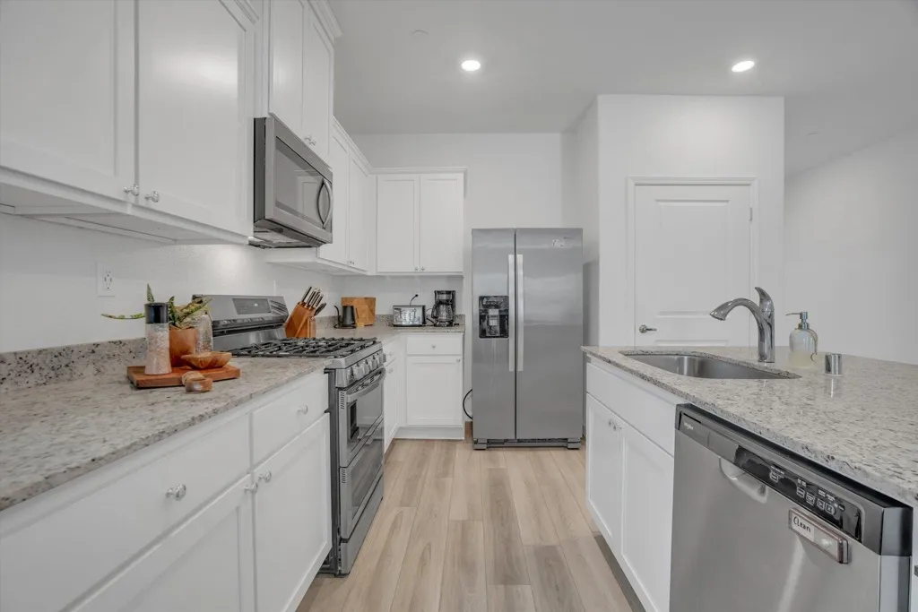 kitchen with stainless steel appliances, light stone counters, white cabinets, light wood-style flooring, and recessed lighting