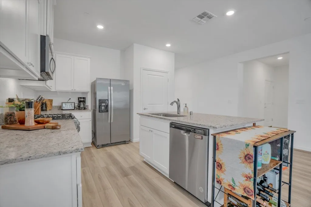 kitchen featuring light wood finished floors, stainless steel appliances, an island with sink, light stone countertops, and white cabinets